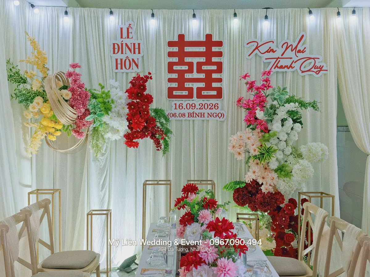 Backdrop lễ đính hôn phông voan trắng, chữ hỷ đỏ và hoa lụa nhiều màu, phía trước là bàn tiệc trà